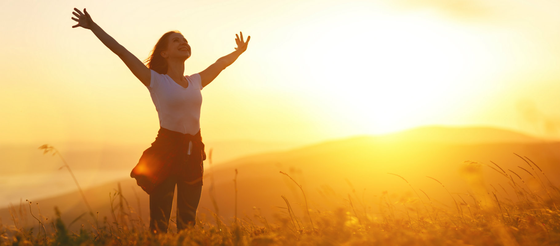 Mujer con los brazos extendidos en la pradera mientras amanece